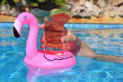 Woman holding a cocktail floating in an inflatable pink flamingo drinks holder, in a swimming pool.