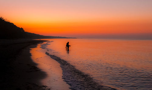 Silhouette man on beach against sky during sunset