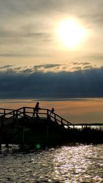 Silhouette people standing on pier over sea against sky during sunset