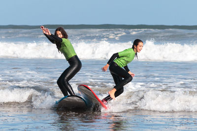 Girls with arms raised surfing in sea against sky