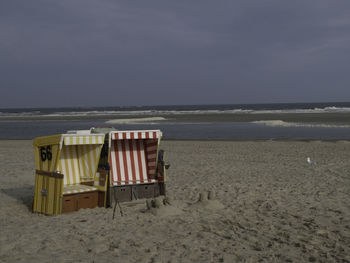 Hooded chairs on beach against sky