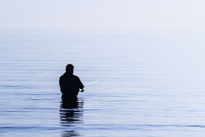 Rear view of silhouette man in sea against sky