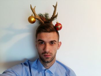 Portrait of man with baubles and antlers against wall