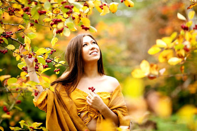 Smiling young woman looking up while standing by fruit trees