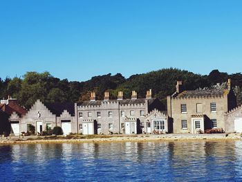 Buildings by river against clear blue sky