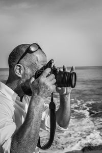 Side view of man photographing with camera by sea