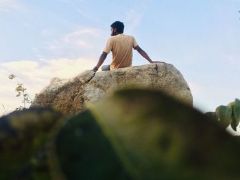 Low angle view of man sitting on rock