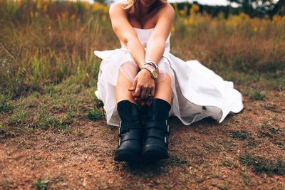 Low section of young woman in wedding dress sitting at park