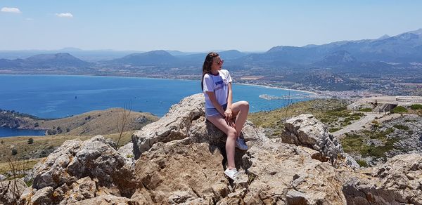 Woman sitting on rock by mountains against sky