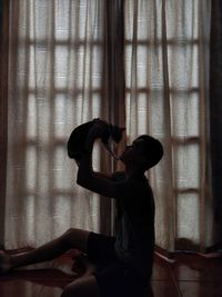 Side view of boy sitting against window at home