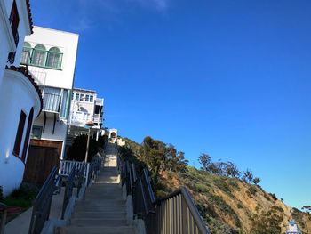 Low angle view of steps amidst buildings against clear blue sky