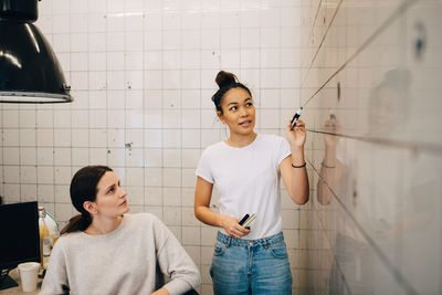 Young computer hacker explaining strategy to female colleague on tile wall at office