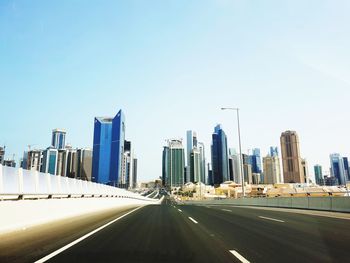 Road by buildings against clear sky