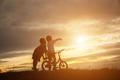 Silhouette people riding bicycle on field against sky during sunset