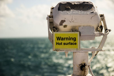 Close-up of information sign by sea against sky