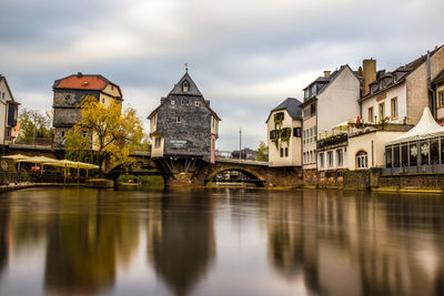 Bridge over river by buildings against sky