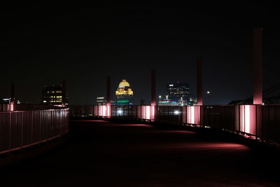 Illuminated street lights by buildings against sky at night