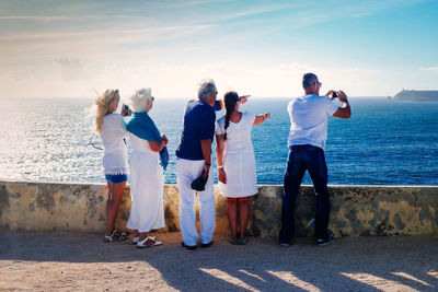 Rear view of people standing on footpath while pointing at sea