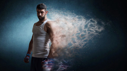 Digital composite image of dissolving boxer standing against blue background