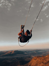 Low angle view of woman swinging against sky during sunset