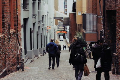 Rear view of people walking on footpath amidst buildings in city