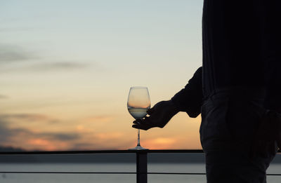 Silhouetted man with white wine glass outdoors at sunset.