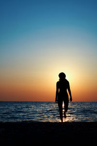 Silhouette woman walking at beach against clear sky during sunset