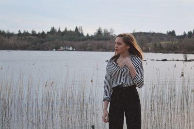 Young woman standing at lakeshore against sky