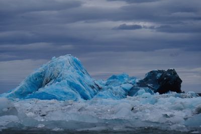 Iceberg in sea against cloudy sky