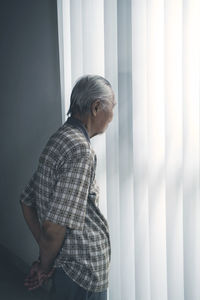 Senior man looking through window while standing at home