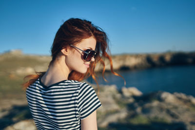 Young woman wearing sunglasses standing against sky