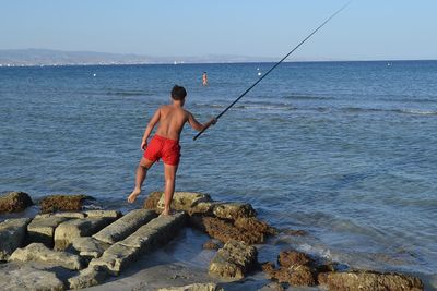 Rear view of shirtless man fishing in sea