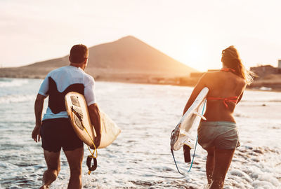 Happy friends carrying surfboards while walking on shore at beach
