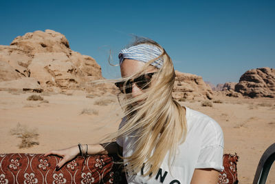 Young woman sitting at desert against clear sky during sunny day