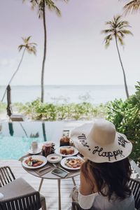 Woman sitting on table by infinity pool against sky