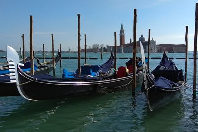 Gondolas moored on grand canal with san giorgio maggiore in background against blue sky