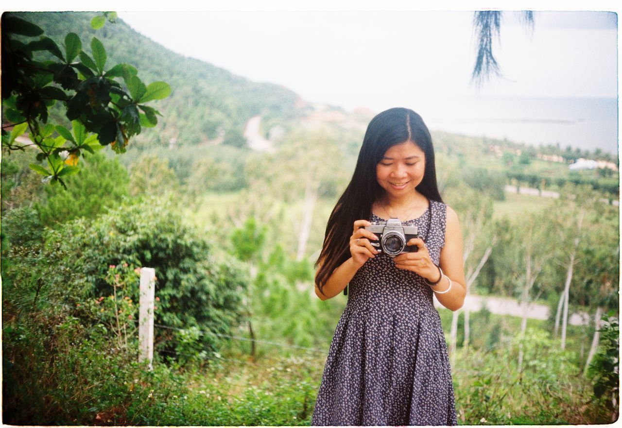 YOUNG WOMAN STANDING AGAINST PLANTS