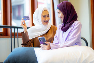 Young woman using phone while sitting on bed at home