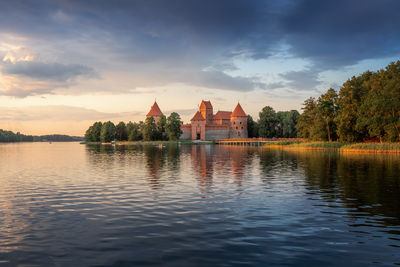 Buildings by lake against sky during sunset