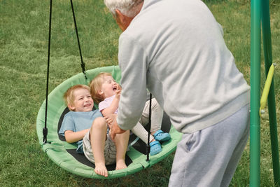 Grandfather swinging children in summer park. grand dad and grandchildren sitting on swing outdoors