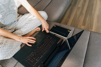 A young woman in pajamas sits on the couch and uses a laptop
