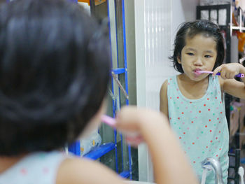 Girl brushing teeth while standing against mirror 