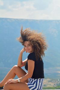 Portrait of smiling young woman sitting on mountain against sky