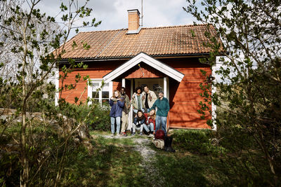 Portrait of happy male and female friends at cottage entrance