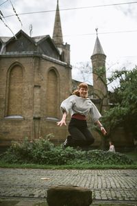 Full length of young woman jumping against built structure