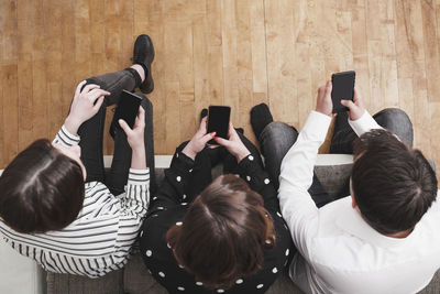 Directly above shot of friends using phones while sitting on hardwood floor