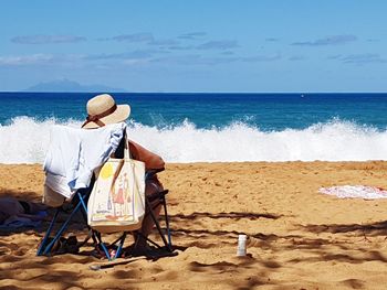 Rear view of man sitting on chair at beach against sky