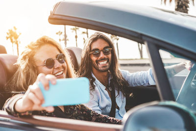 Happy woman taking selfie with boyfriend while sitting in convertible