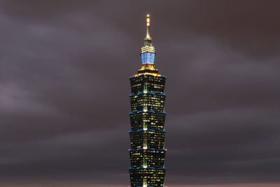 Illuminated tower against cloudy sky at night