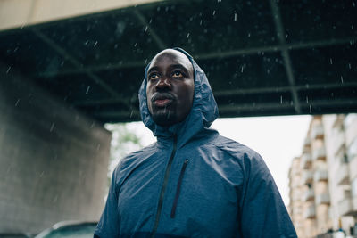 Low angle view of sportsman looking away while standing against bridge during rainy season